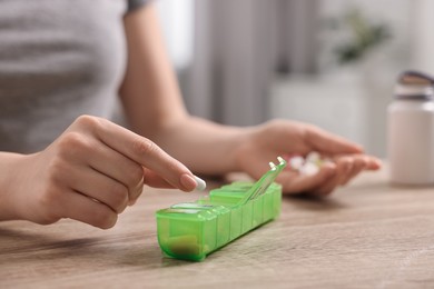 Photo of Woman with pills and organizer at wooden table, closeup