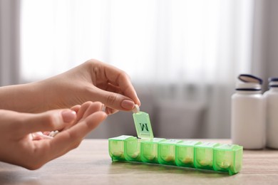 Photo of Woman with pills and organizer at wooden table, closeup