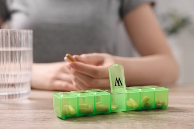 Photo of Woman with pills, organizer and glass of water at wooden table, closeup