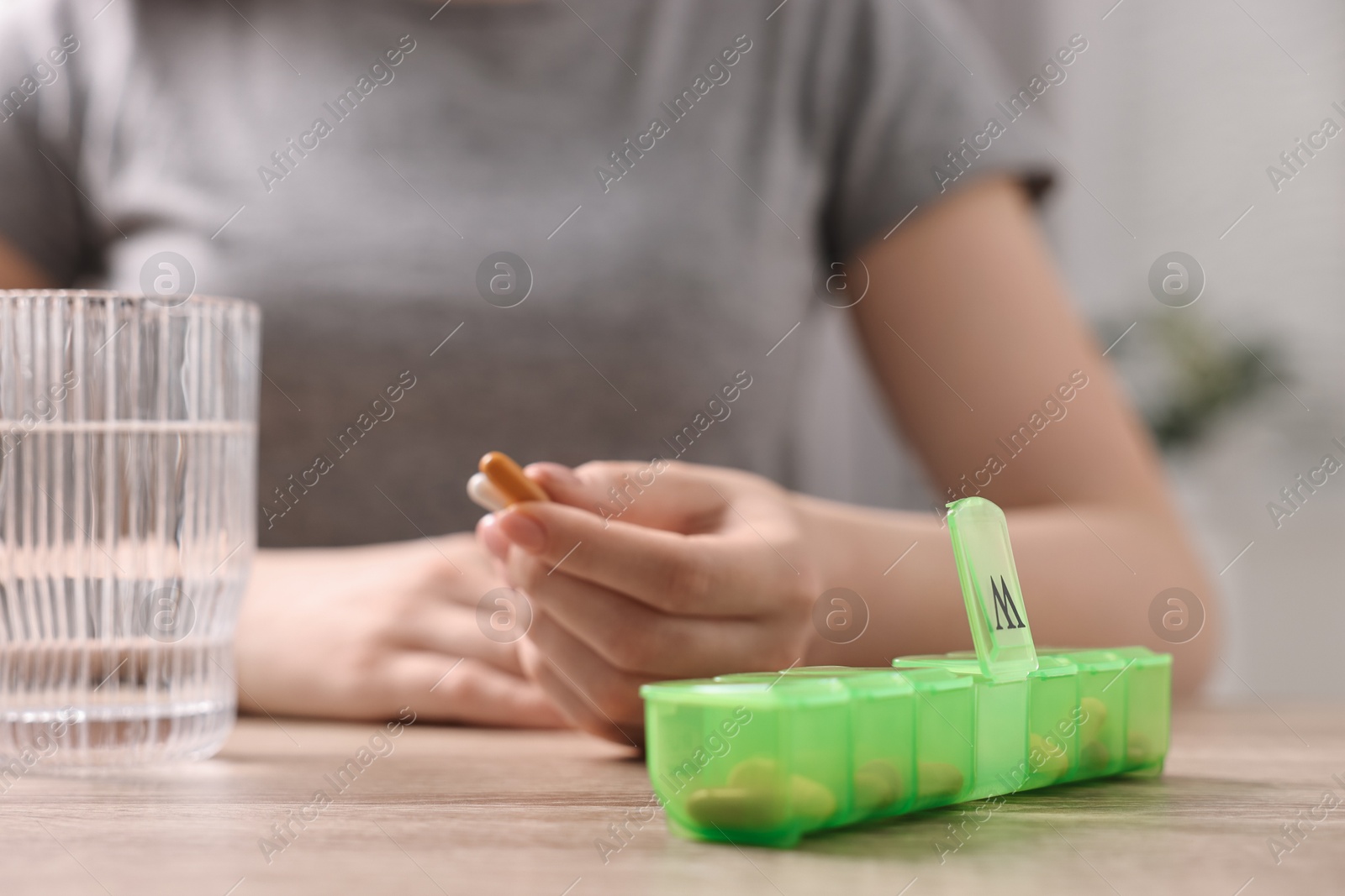 Photo of Woman with pills, organizer and glass of water at wooden table, closeup