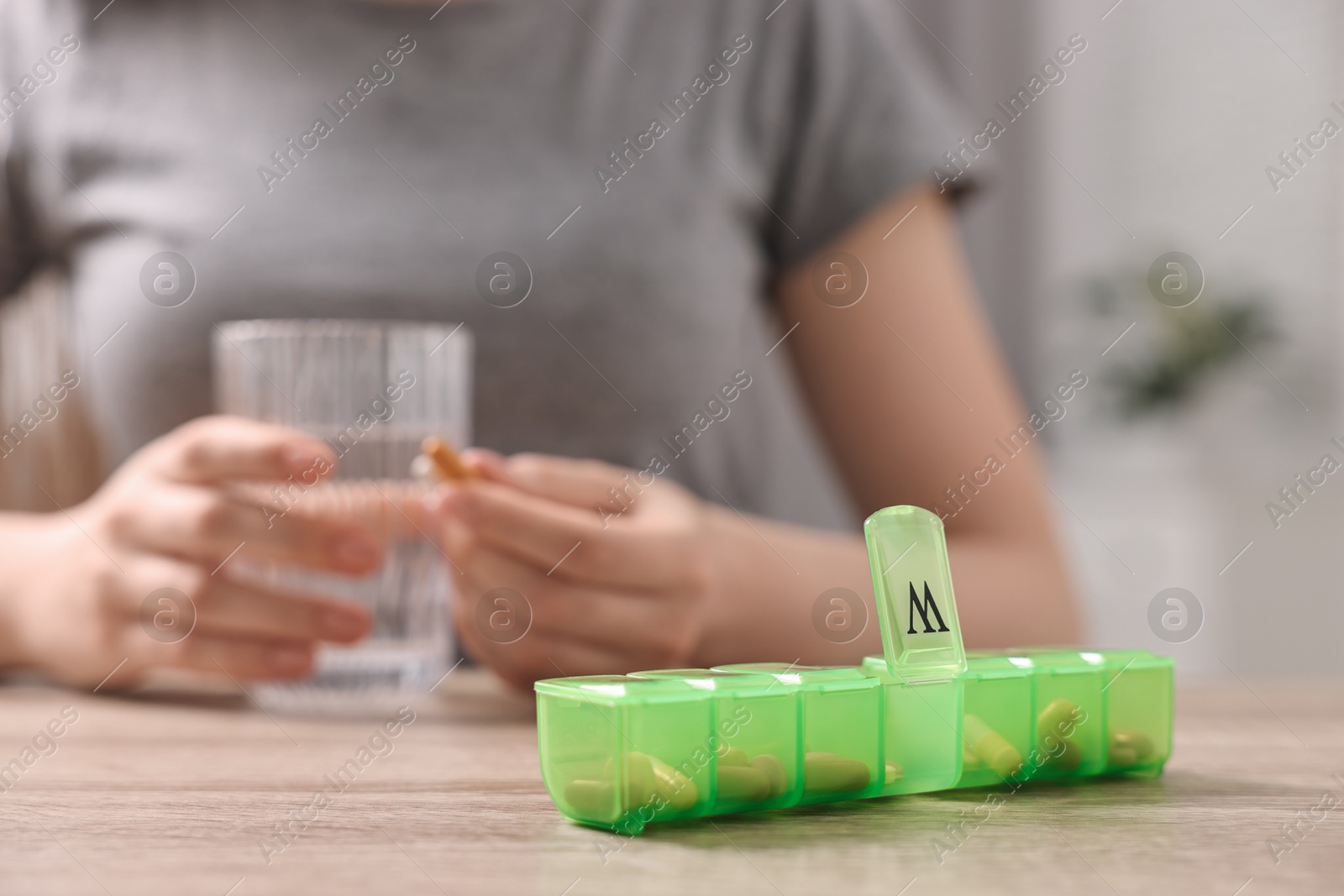 Photo of Woman with pills, organizer and glass of water at wooden table, closeup