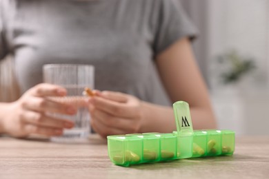 Woman with pills, organizer and glass of water at wooden table, closeup