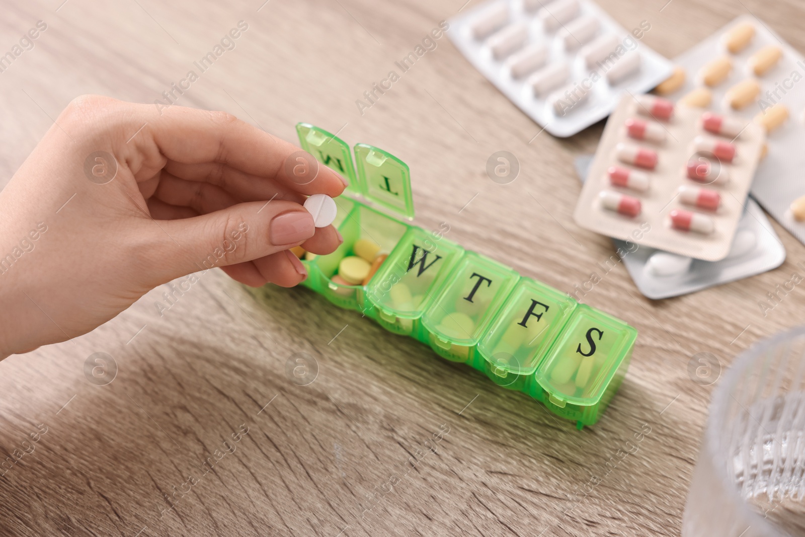 Photo of Woman with pills, organizer and glass of water at wooden table, closeup