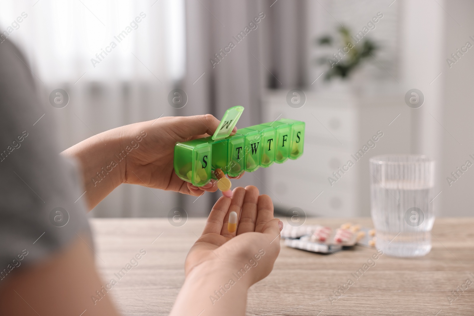 Photo of Woman with pills, organizer and glass of water at wooden table, closeup