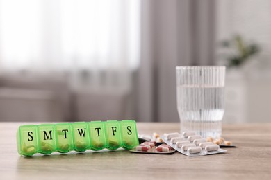 Different pills, organizer and glass of water at wooden table, closeup. Space for text