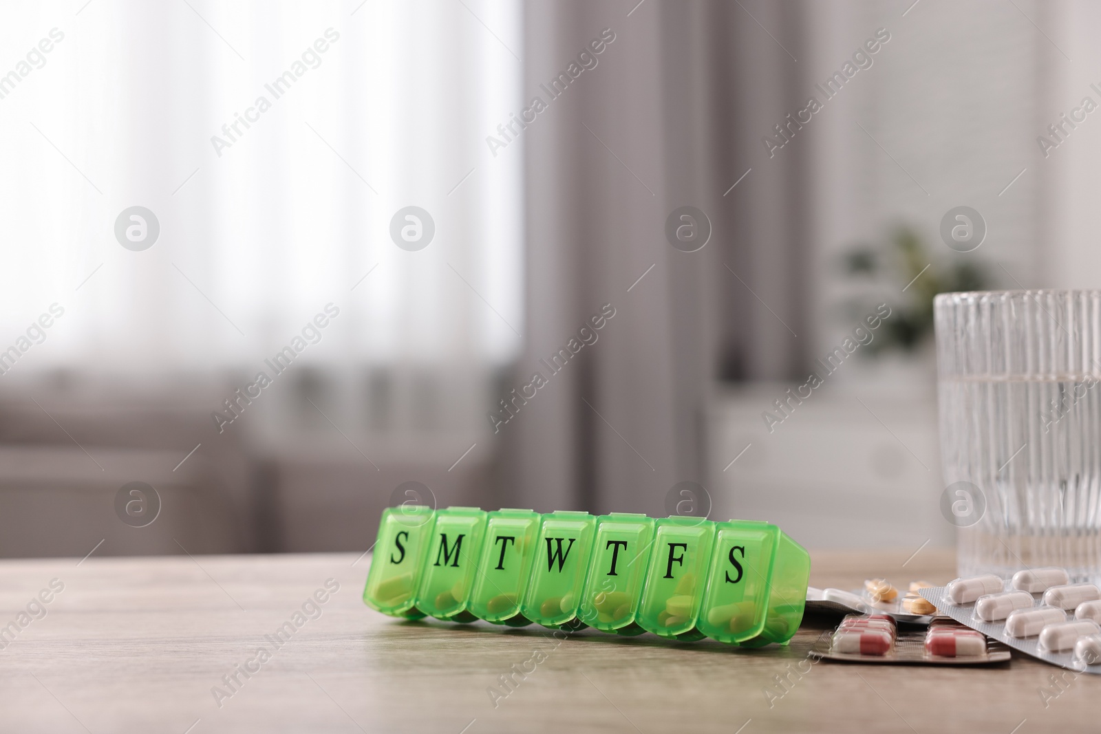 Photo of Different pills, organizer and glass of water at wooden table, closeup. Space for text