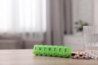 Photo of Different pills, organizer and glass of water at wooden table, closeup. Space for text