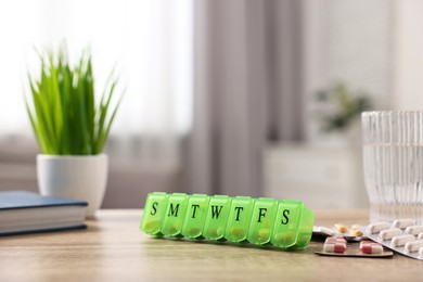 Photo of Different pills, organizer and glass of water at wooden table, closeup. Space for text