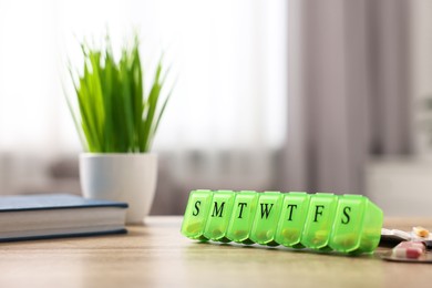 Photo of Different pills and organizer at wooden table, closeup