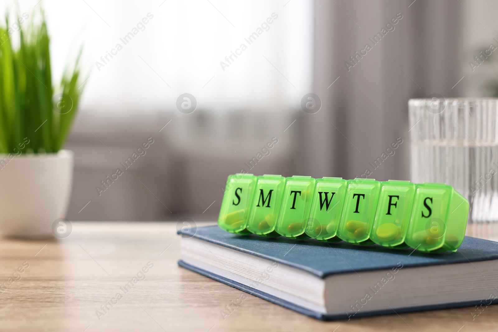 Photo of Different pills in organizer and glass of water at wooden table, closeup. Space for text