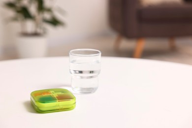 Different pills in organizer and glass of water at white table, closeup. Space for text