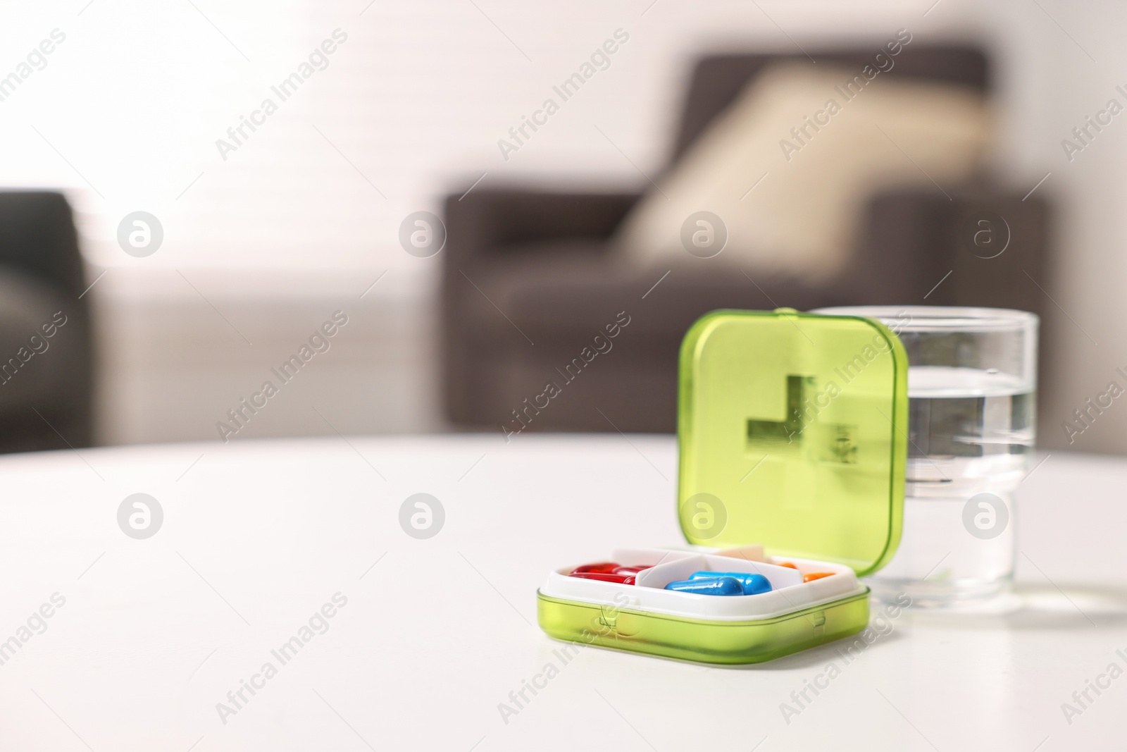 Photo of Different pills in organizer and glass of water at white table, closeup. Space for text