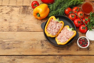 Raw stuffed peppers with ground meat and ingredients on wooden table, flat lay. Space for text