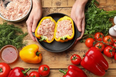 Woman making stuffed peppers with ground meat at wooden table, top view