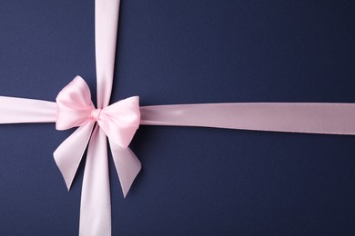 Photo of Pink satin ribbon with bow on blue background, top view