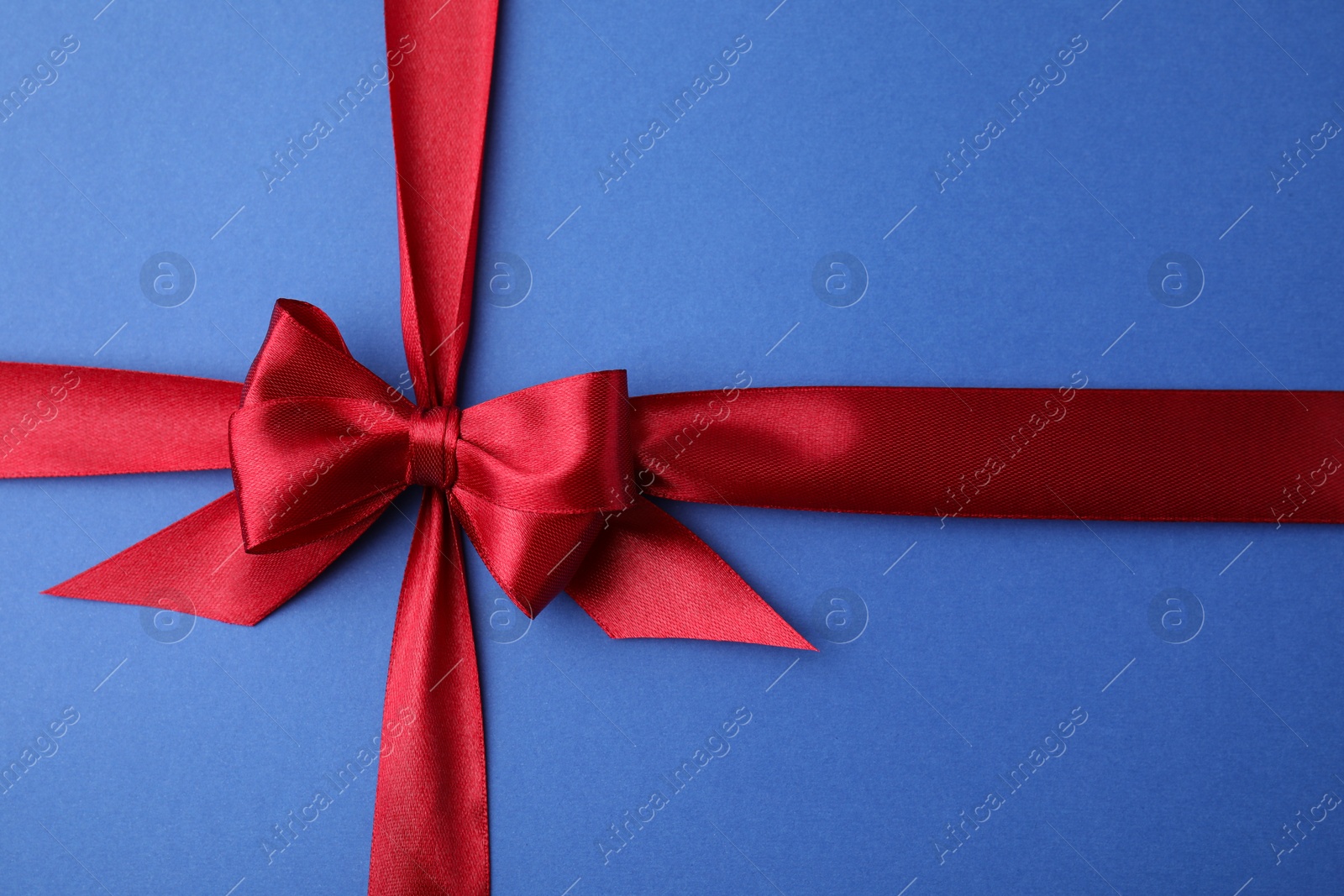 Photo of Red satin ribbon with bow on blue background, top view