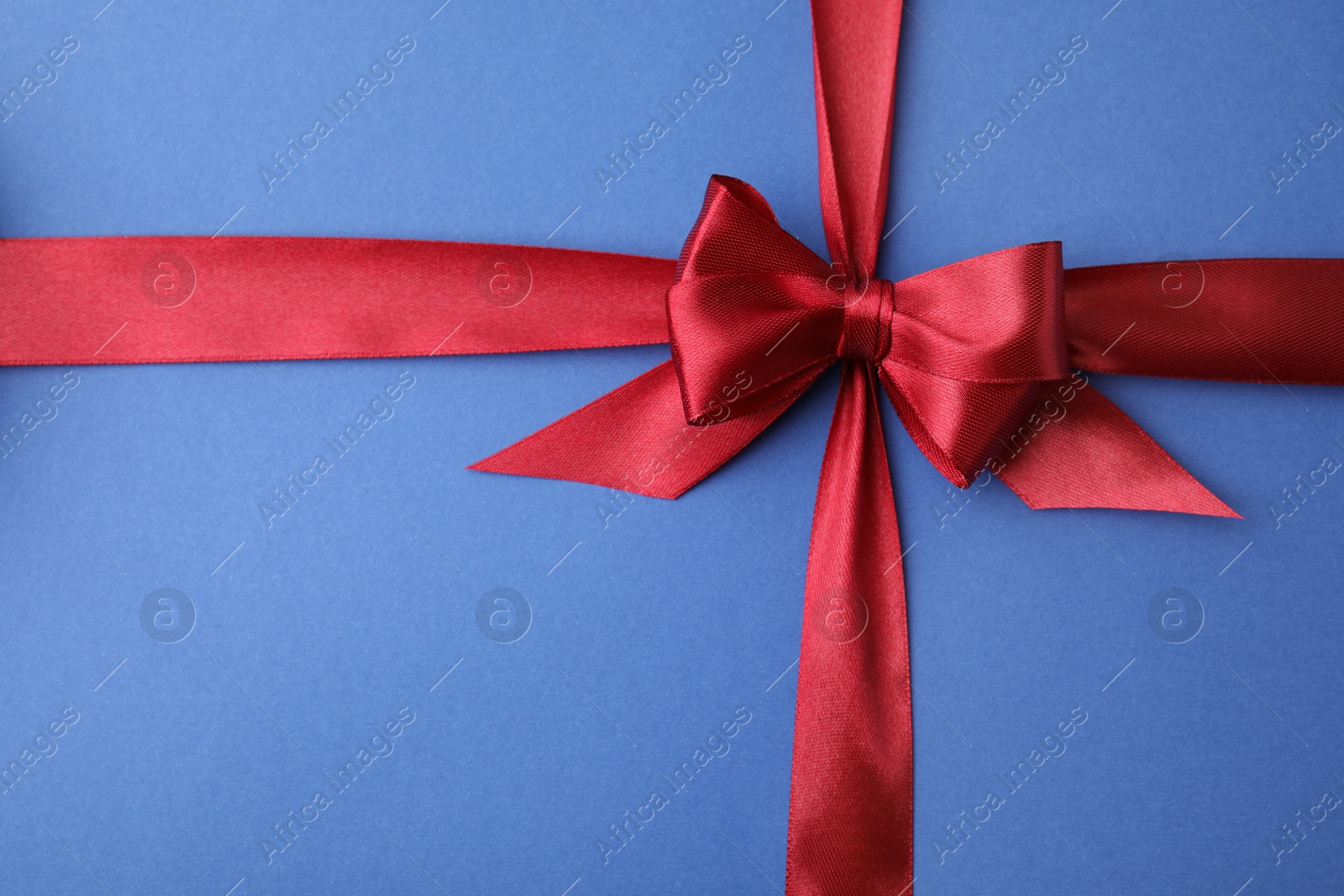 Photo of Red satin ribbon with bow on blue background, top view