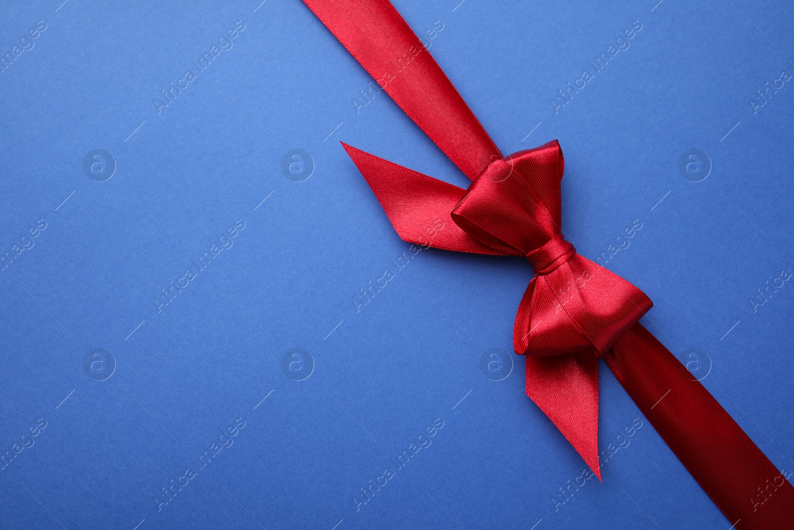 Photo of Red satin ribbon with bow on blue background, top view. Space for text