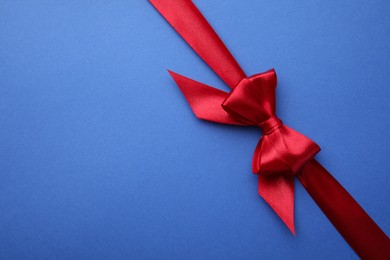 Red satin ribbon with bow on blue background, top view. Space for text