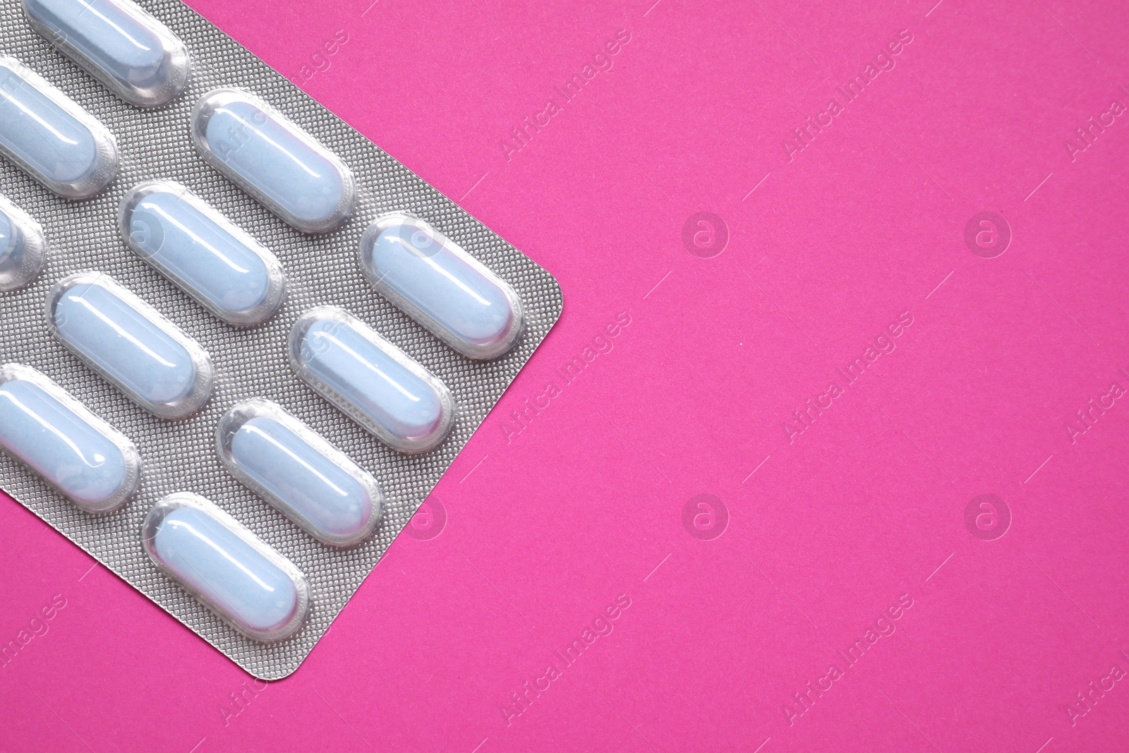 Photo of Pills in blister on pink background, top view. Space for text