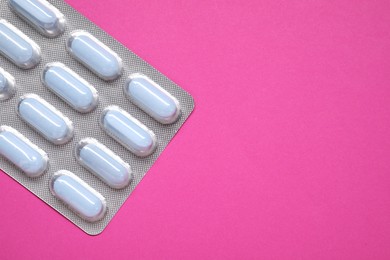 Photo of Pills in blister on pink background, top view. Space for text