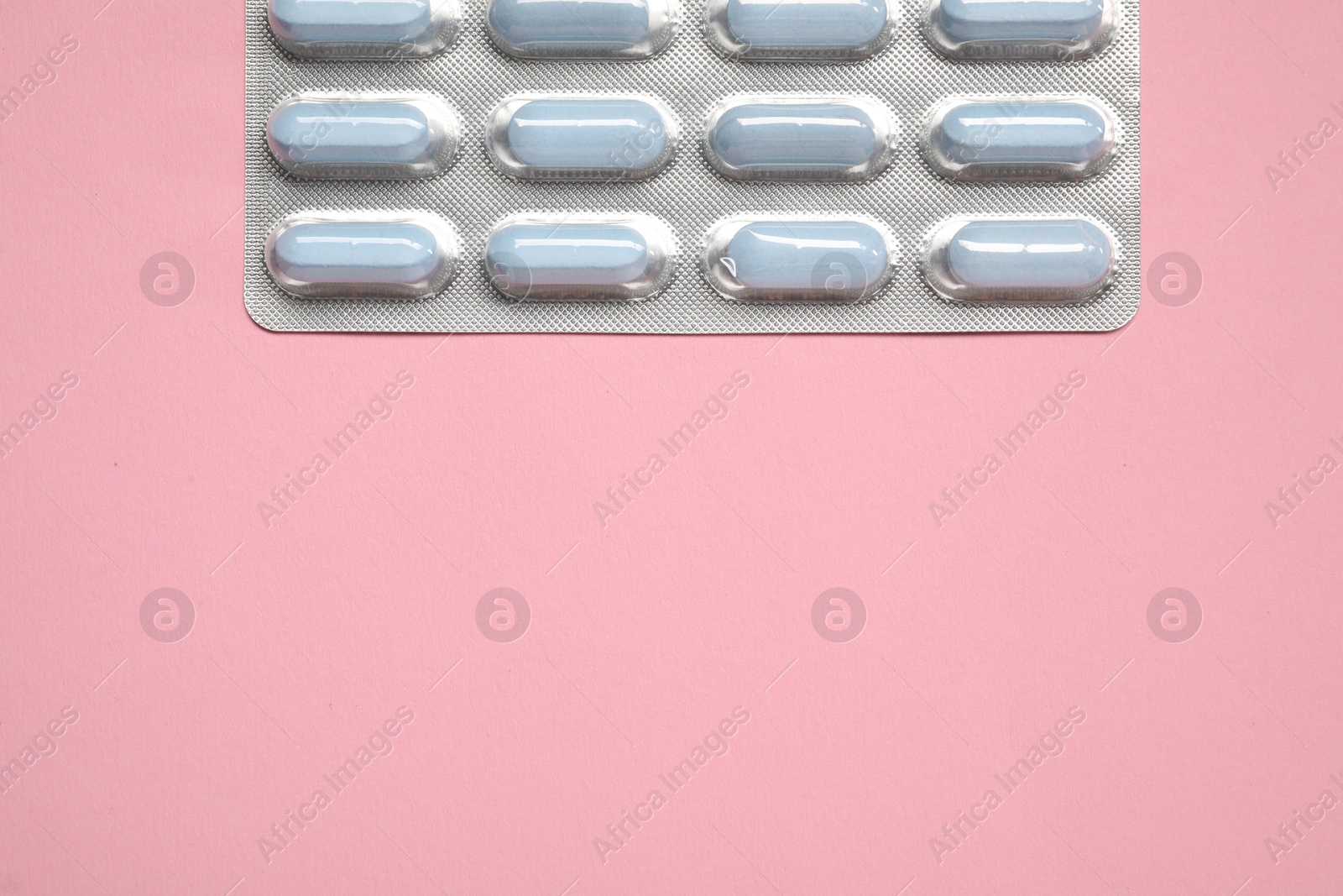 Photo of Pills in blister on pink background, top view. Space for text