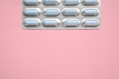 Pills in blister on pink background, top view. Space for text