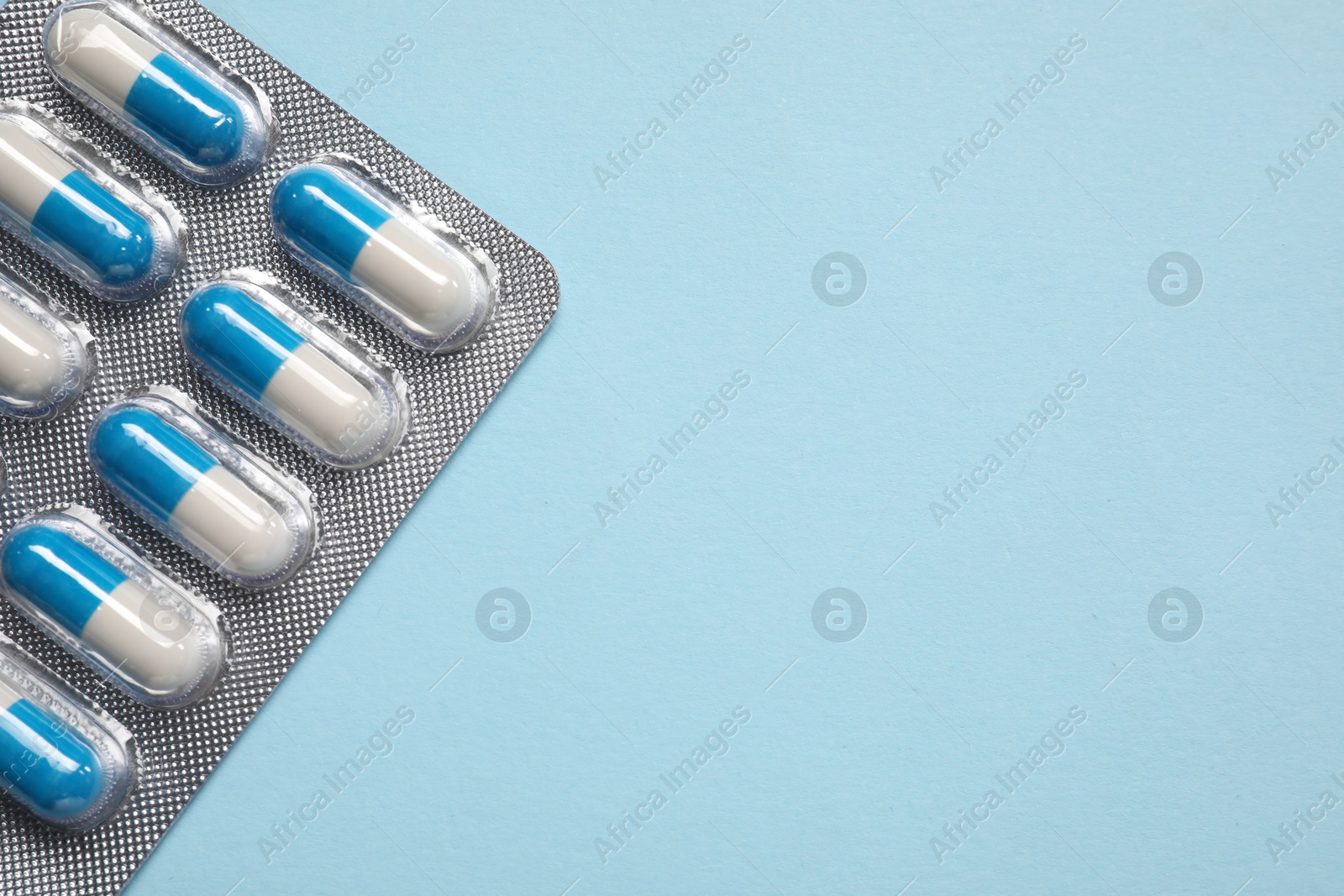 Photo of Antibiotic pills in blister on light blue background, top view. Space for text