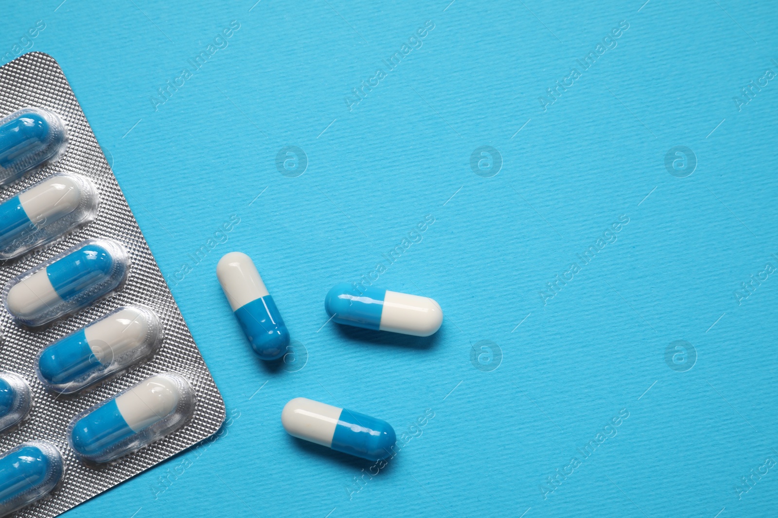 Photo of Antibiotic pills in blister on light blue background, top view. Space for text