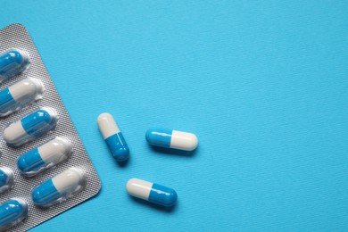 Photo of Antibiotic pills in blister on light blue background, top view. Space for text