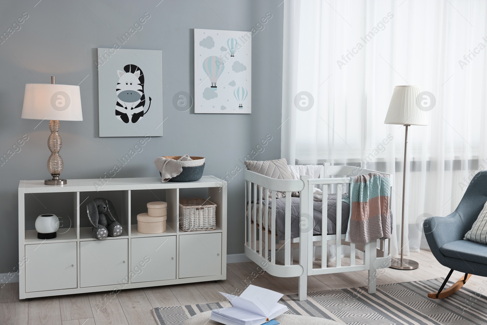 Photo of Newborn baby room interior with stylish furniture, comfortable crib and pictures of on wall