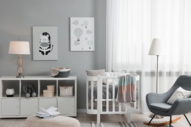 Newborn baby room interior with stylish furniture, comfortable crib and pictures of on wall