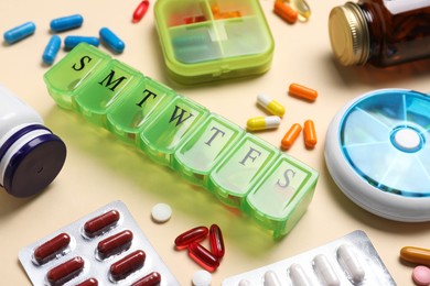 Photo of Different pills, organizers and medical jars on beige background, closeup