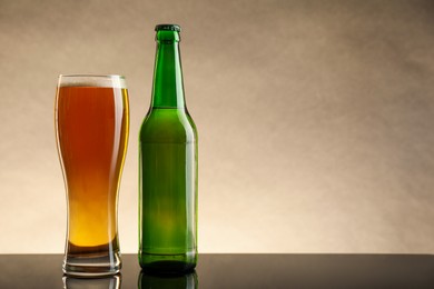 Photo of Bottle and glass of beer on table against beige background. Space for text