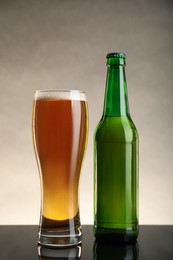 Photo of Bottle and glass of beer on table against beige background