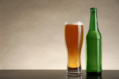 Bottle and glass of beer on table against beige background. Space for text