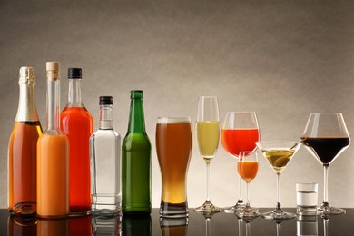 Bottles and glasses with different alcoholic drinks on table against beige background