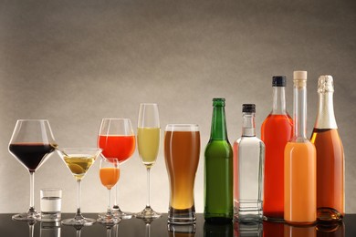 Bottles and glasses with different alcoholic drinks on table against beige background