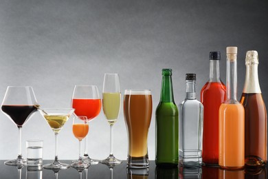 Bottles and glasses with different alcoholic drinks on table against light grey background