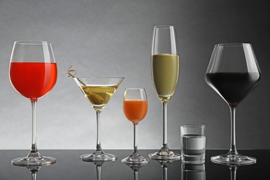 Glasses with different alcoholic drinks on table against light grey background