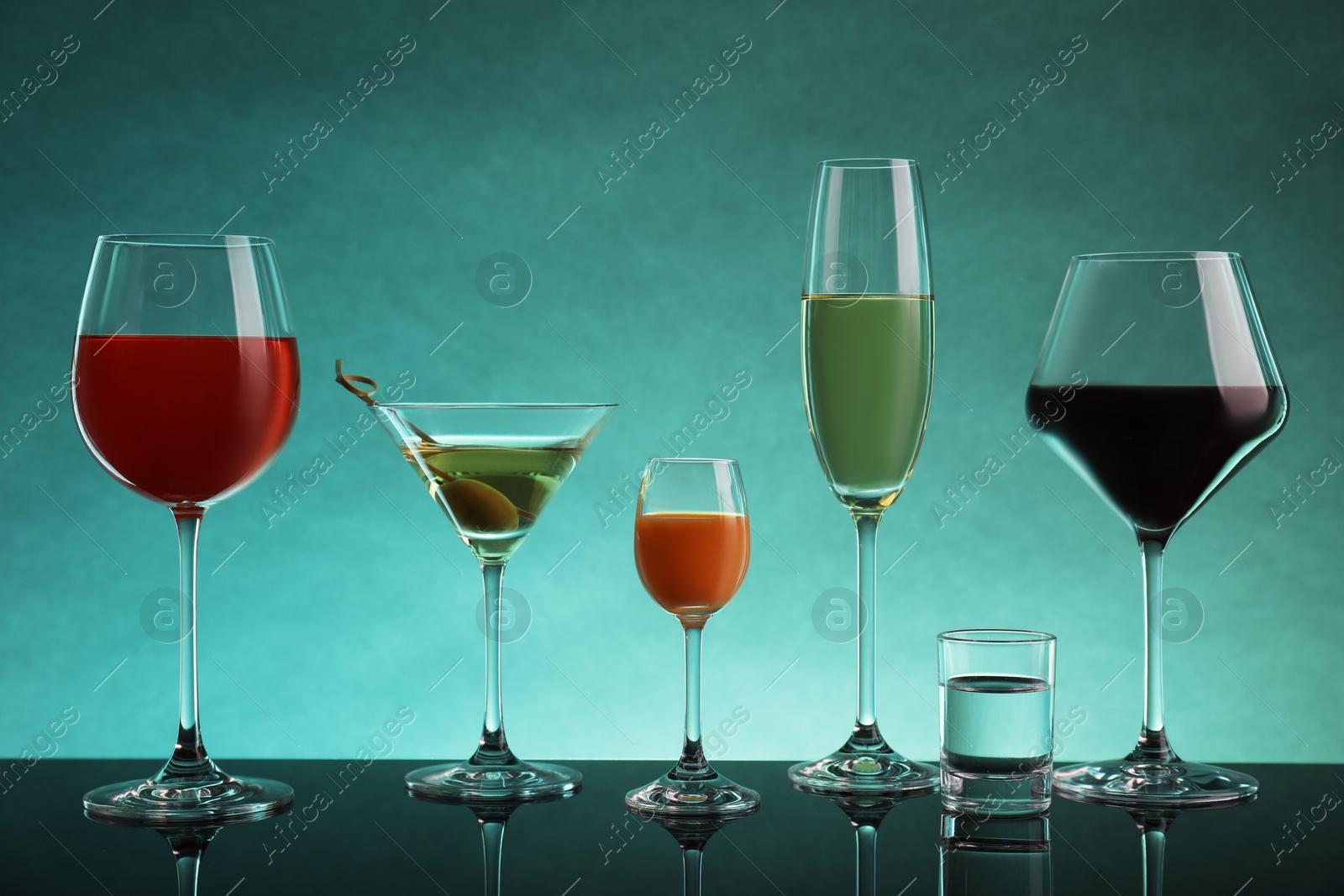 Photo of Glasses with different alcoholic drinks on table against turquoise background