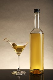 Photo of Bottle of alcoholic drink and martini glass with cocktail on table against beige background