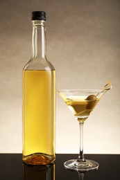 Photo of Bottle of alcoholic drink and martini glass with cocktail on table against beige background