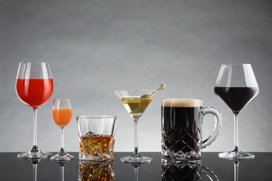 Glasses with different alcoholic drinks on table against light grey background