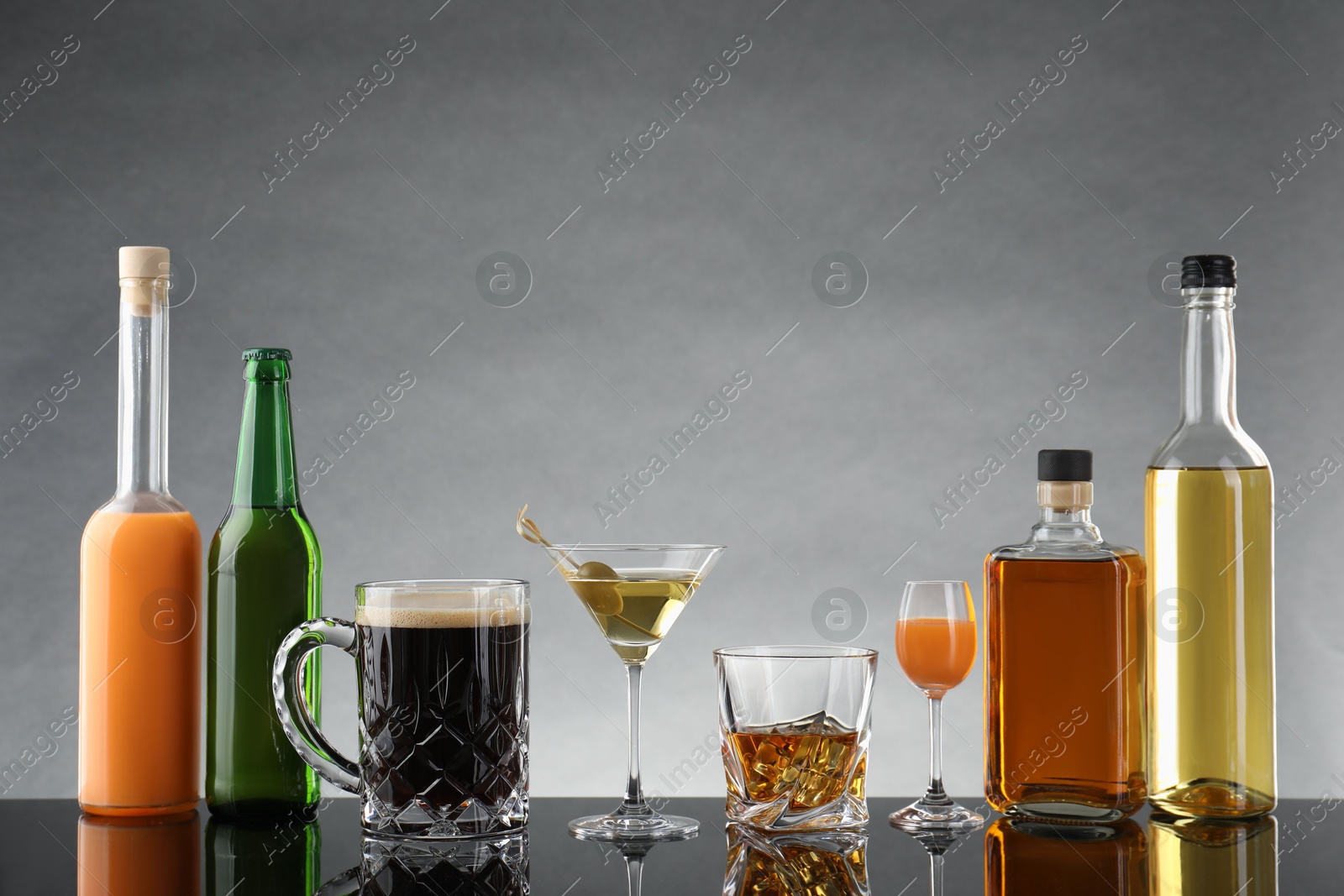 Photo of Bottles and glasses with different alcoholic drinks on table against light grey background