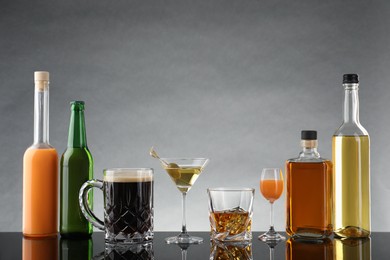 Bottles and glasses with different alcoholic drinks on table against light grey background