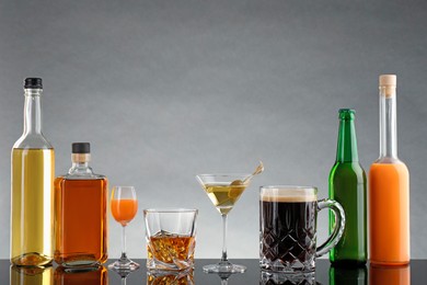 Bottles and glasses with different alcoholic drinks on table against light grey background