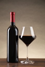 Photo of Bottle and glass of red wine on wooden table against beige background