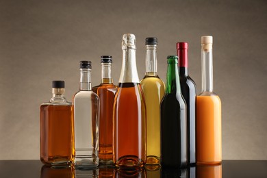 Bottles with different alcoholic drinks on table against beige background