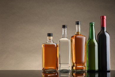 Photo of Bottles with different alcoholic drinks on table against beige background. Space for text